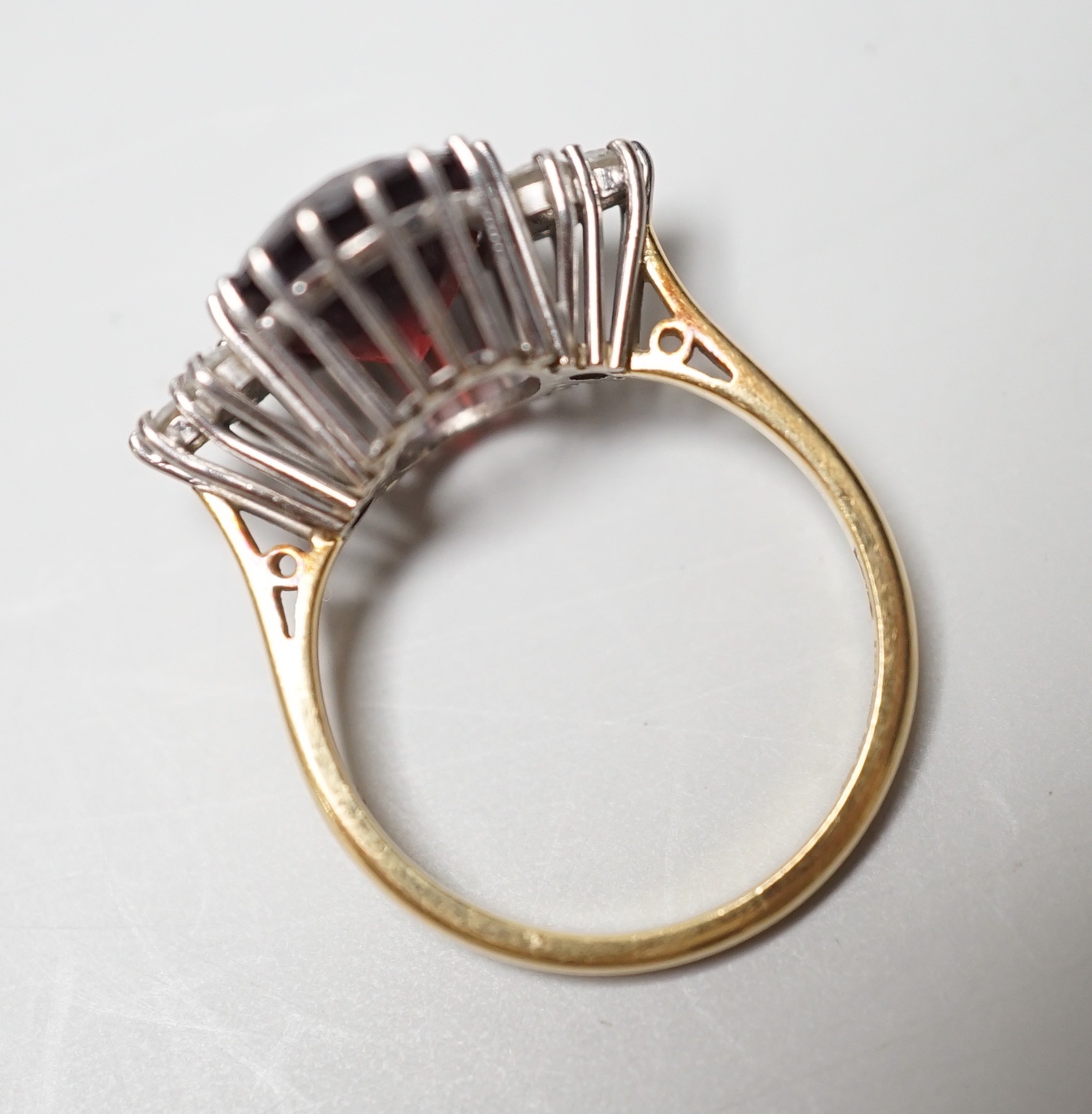 A modern 18ct gold and oval cut garnet set dress ring, with six stone diamond set shoulders, size M/N, gross weight 4.8 grams.